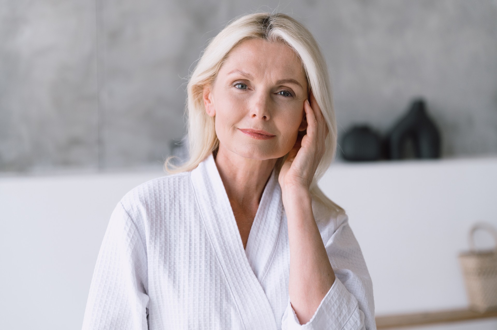 Matured woman in white bathrobe touching her perfect skin