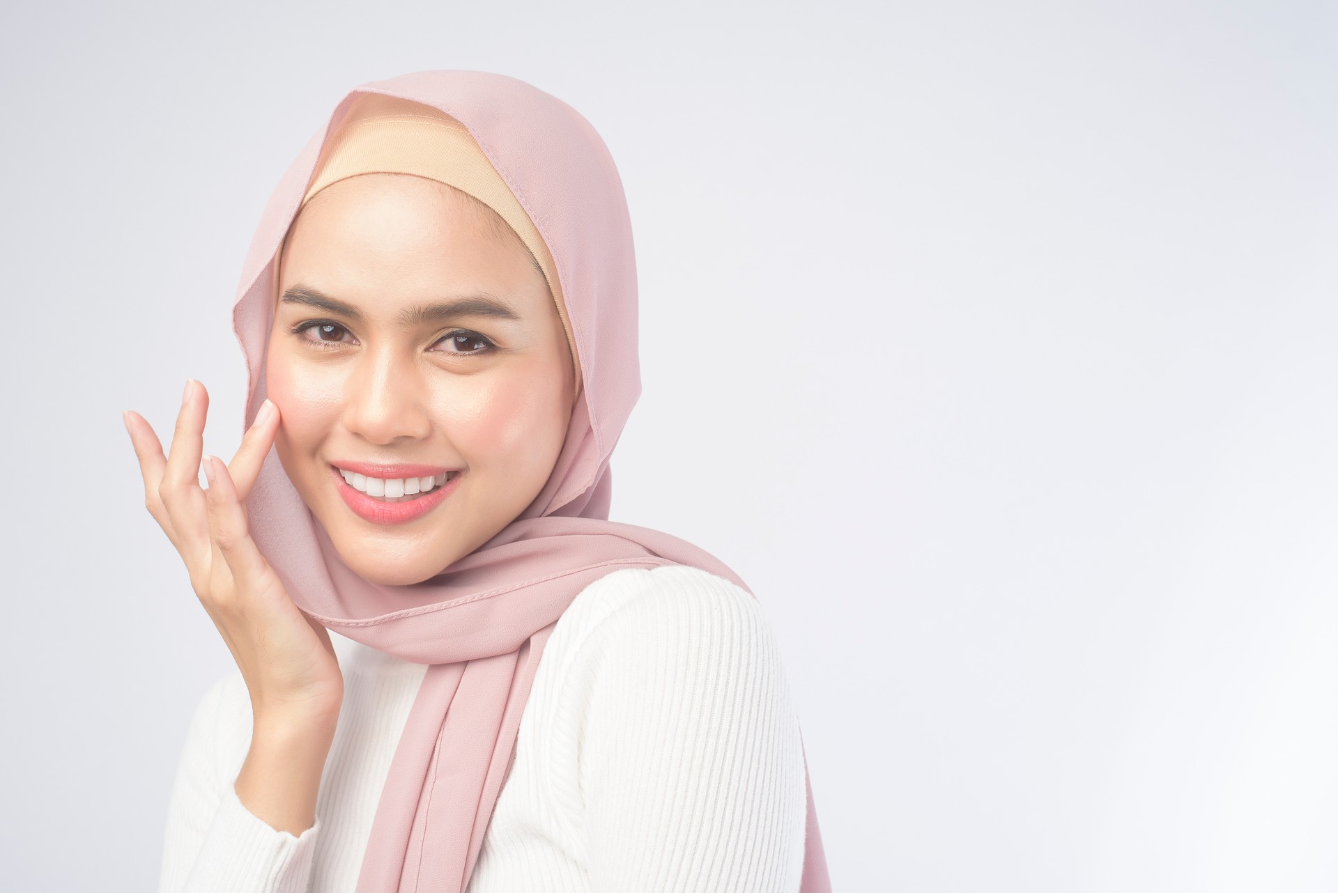 Portrait of young smiling muslim woman wearing a pink hijab over white background studio.